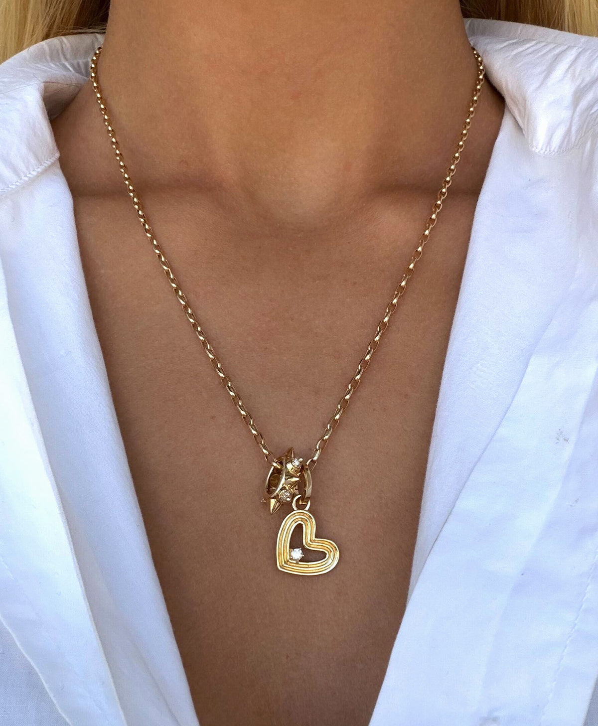 A gold necklace with a heart-shaped pendant and a big bead pendant, worn by a model in a white collared shirt.