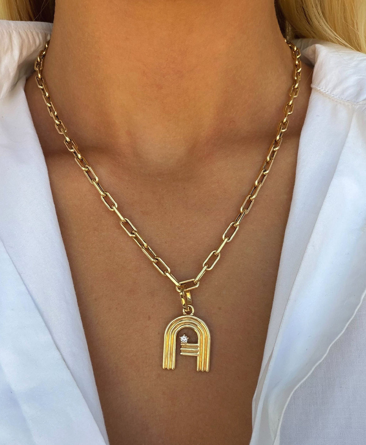 A gold chain necklace with a letter 'A' charm with a small diamond, worn by a model in a white collared shirt.