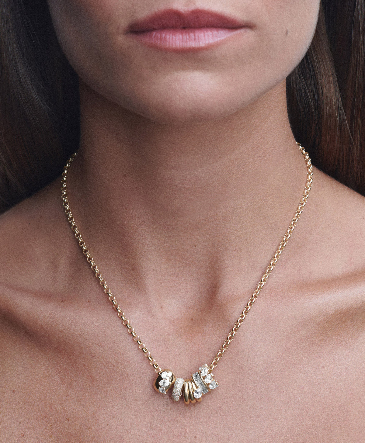 A close-up of a model's neck and chest wearing a delicate gold chain necklace with a cluster of give big beads with diamonds.