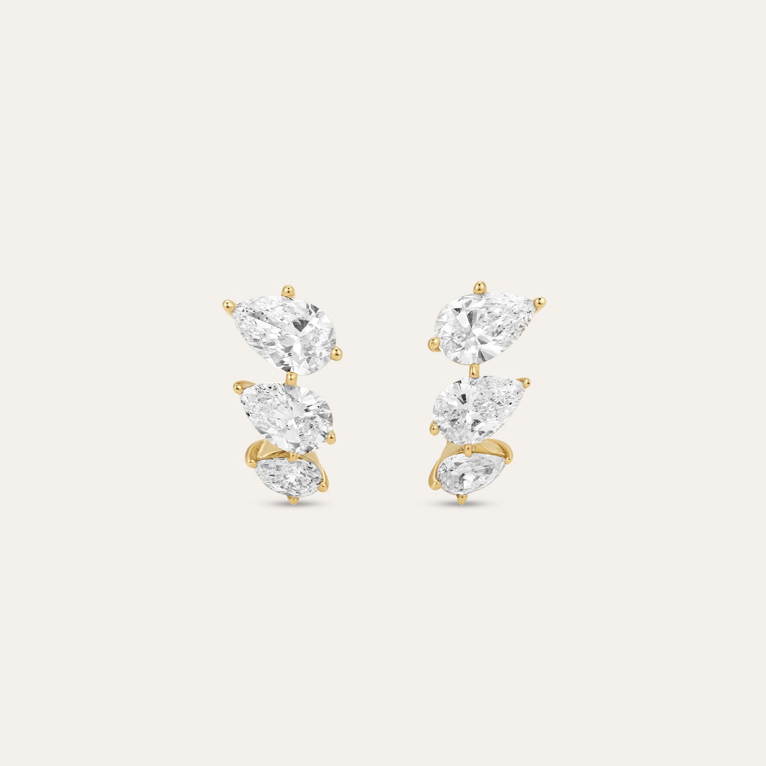 A pair of gold and diamond stud earrings featuring a cascading arrangement of prong setting, shown against a light beige background.