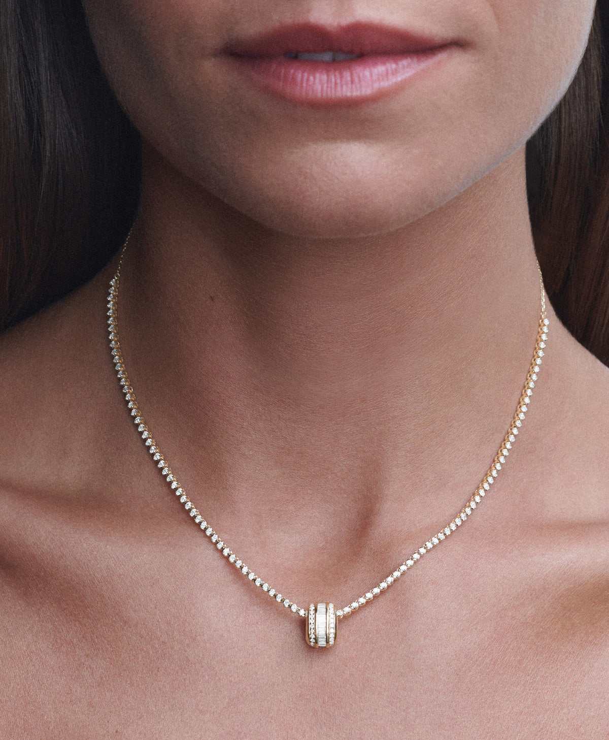 A close-up of a model's neck and lower face wearing a delicate diamond chain necklace with a diamond big bead pendant.