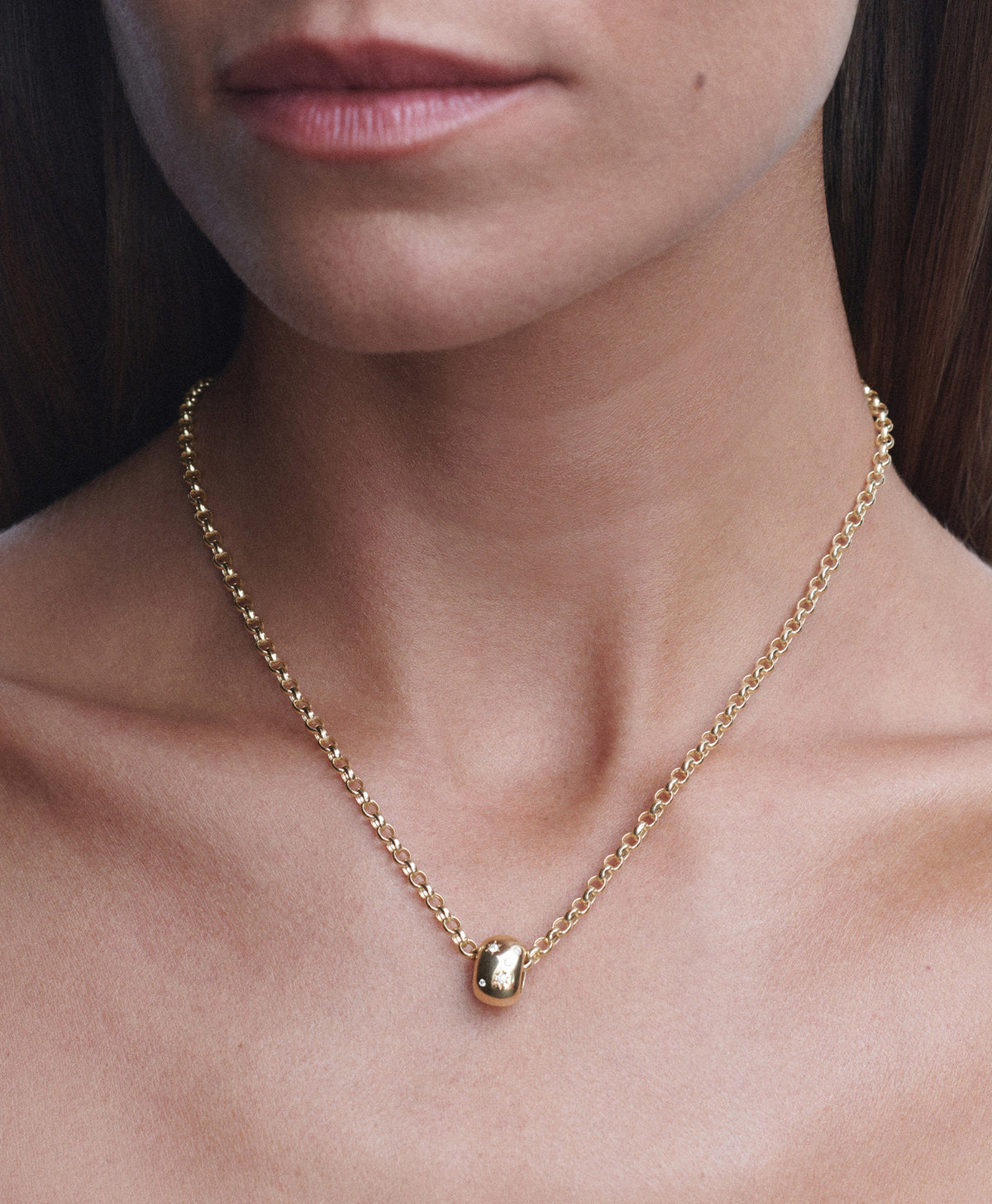 A close-up of a model's neck and chest wearing a delicate gold chain necklace with a small polished gold pendant.