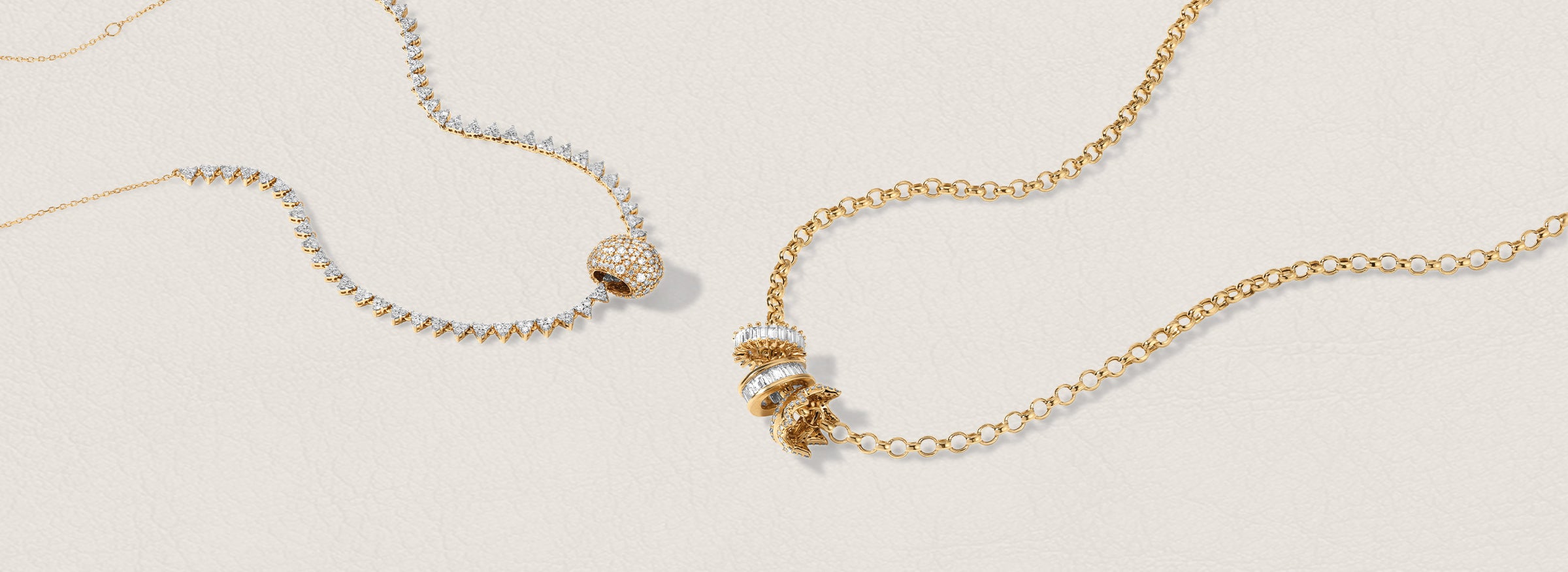 Two chain necklaces one in gold and one with diamonds, displayed on a light beige background. One necklace features one diamond bead, while the other has a cluster of three big beads with diamonds