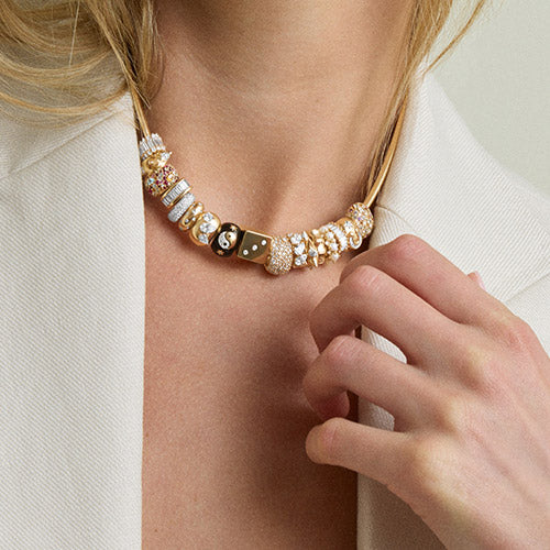 A woman with blonde hair wearing a cream blazer and a gold necklace with various big beads accented in different designs with beads.
